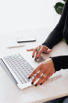 About A businesswoman's hands typing on a laptop at a bright, modern workspace.